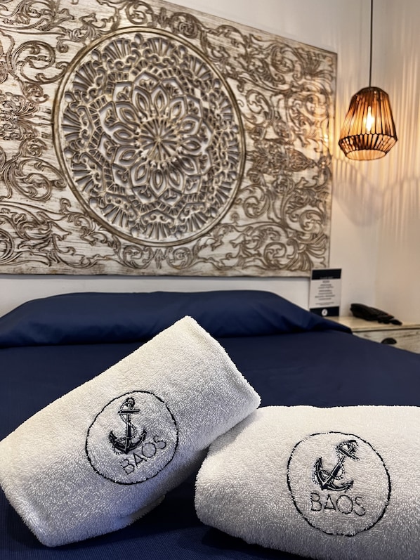 Una cama con ropa de cama azul marino y dos toallas blancas con el bordado 'BAOS'.