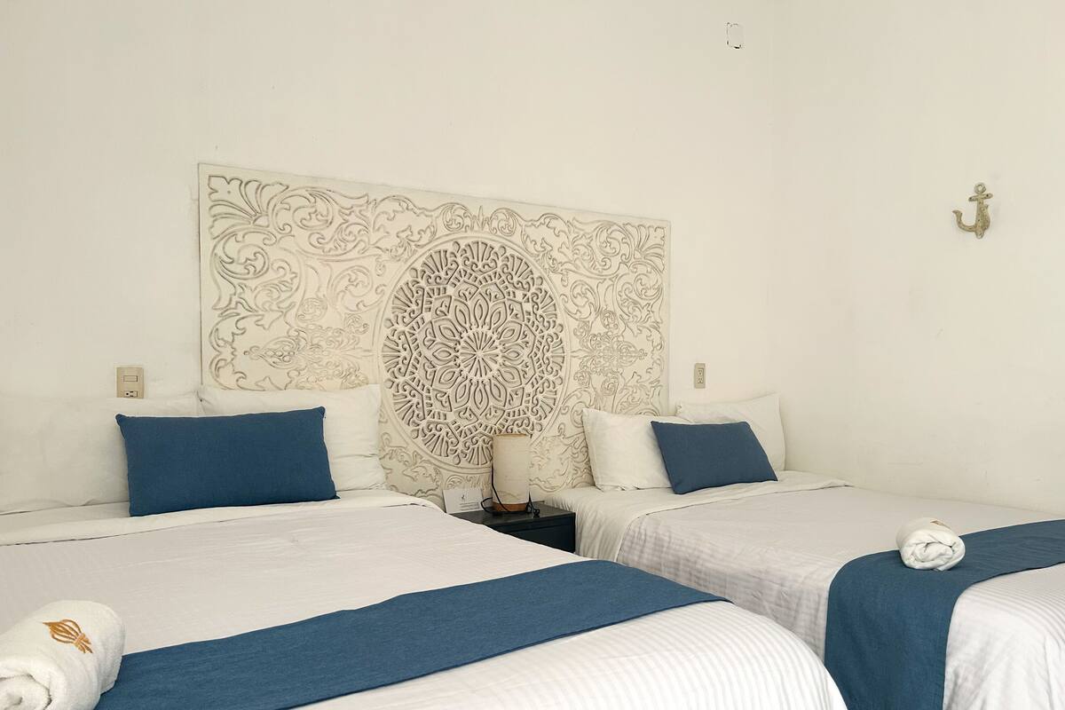 A hotel room with two beds, each with a blue bedspread and white bedding. There is a decorative wall panel above the beds.