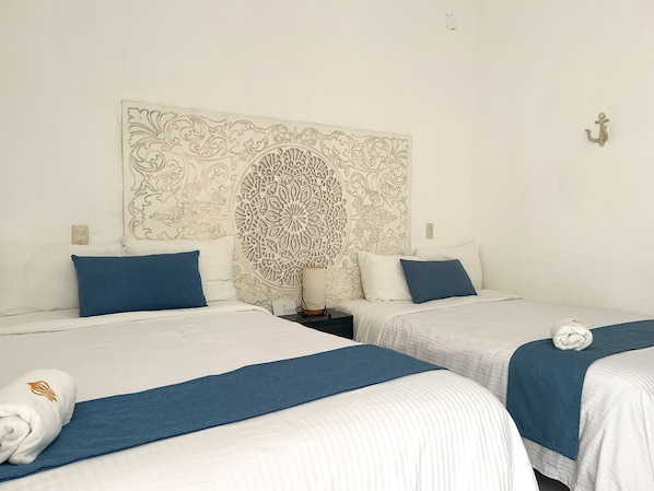 Une chambre d’hôtel avec deux lits, chacun recouvert d’une couvre-lit bleue et doté de draps blancs. Un panneau décoratif orne le mur au-dessus des lits.