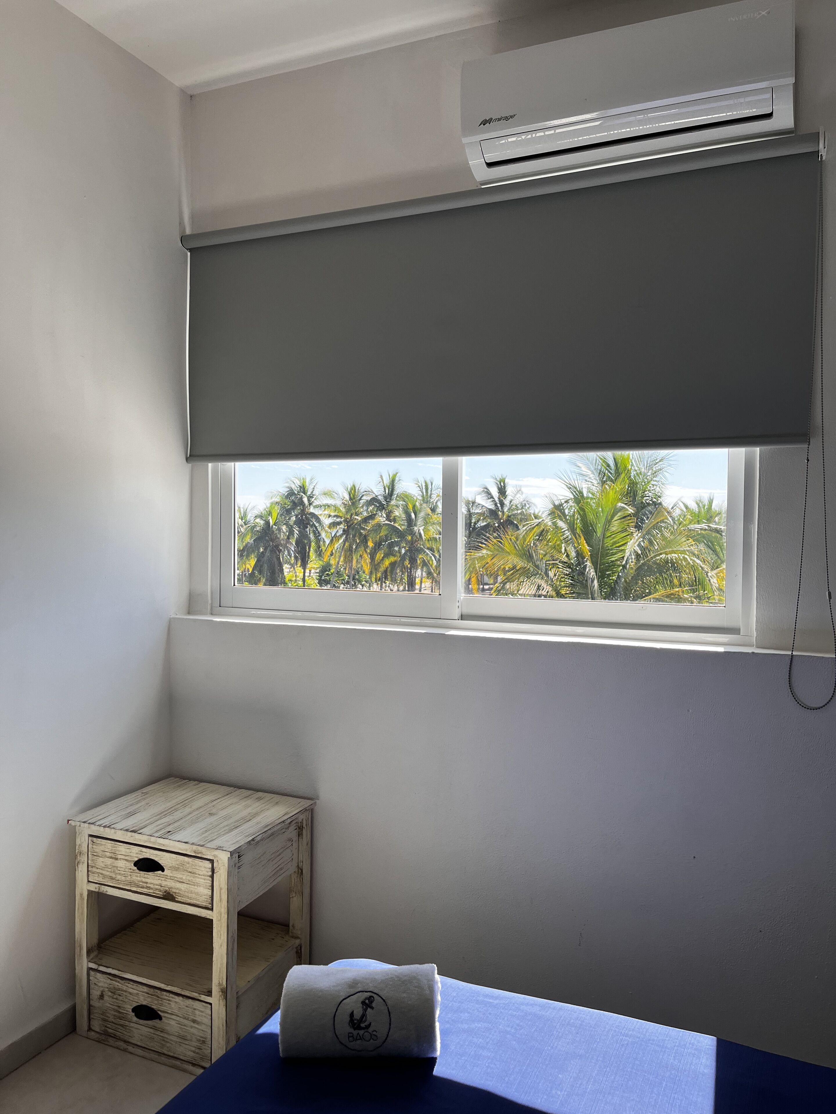 A room with a window, a small wooden cabinet, and a towel on a bed.
