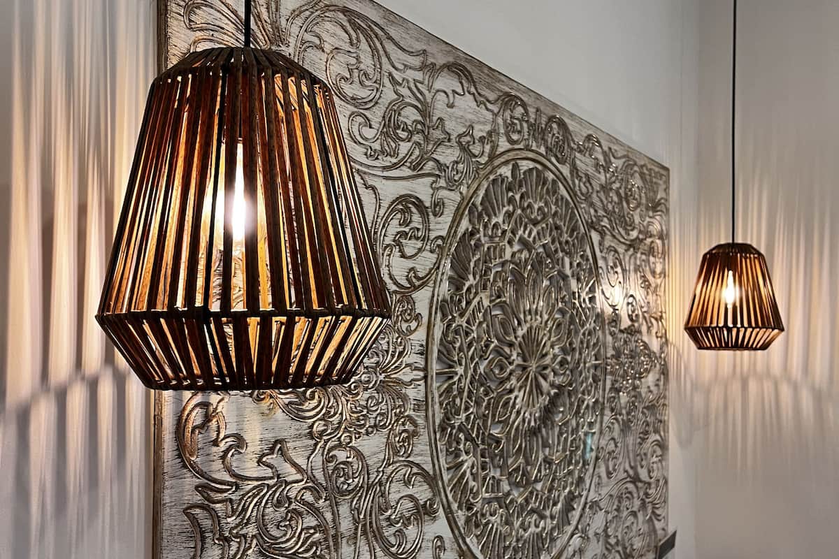 A bedroom with a large wall-mounted artwork, two hanging pendant lights, and a neatly made bed.