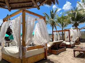 Un cabanon de plage avec une structure en bois et un auvent en tissu blanc, entouré de palmiers et de chaises de plage.