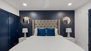 Ein modernes Schlafzimmer mit einem großen Bett, zwei Nachttischen mit Lampen und dekorativen Spiegeln an den Wänden.