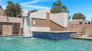 Ein Schwimmbecken mit einer Springbrunnenanlage, einer gefliesten Liegefläche und einem Stuhl.