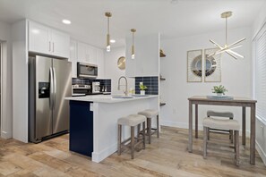 Una cocina moderna con armarios blancos, electrodomésticos de acero inoxidable y una isla central con taburetes.