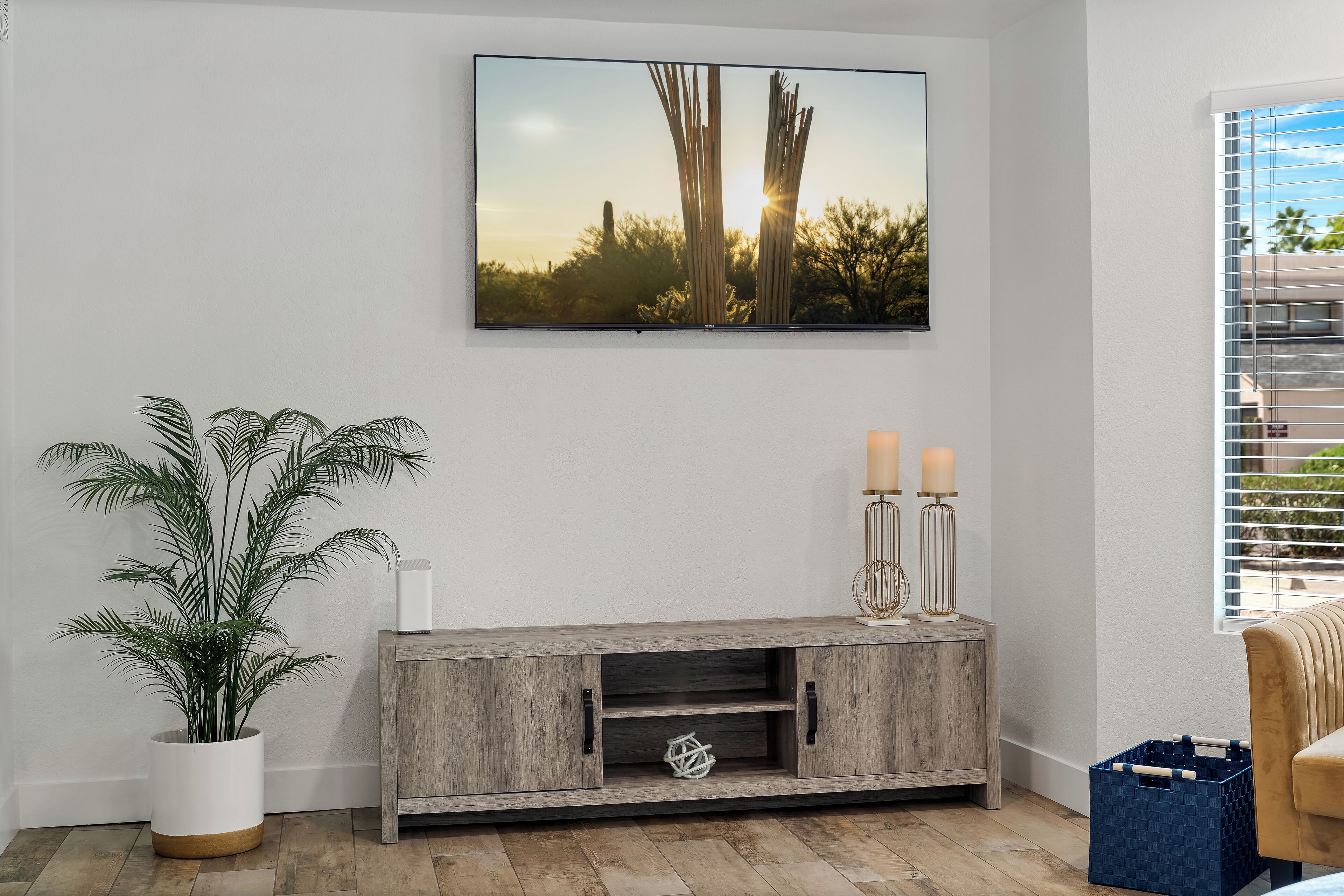 A living room with a mounted TV, a wooden console, a potted plant, and a window with blinds.