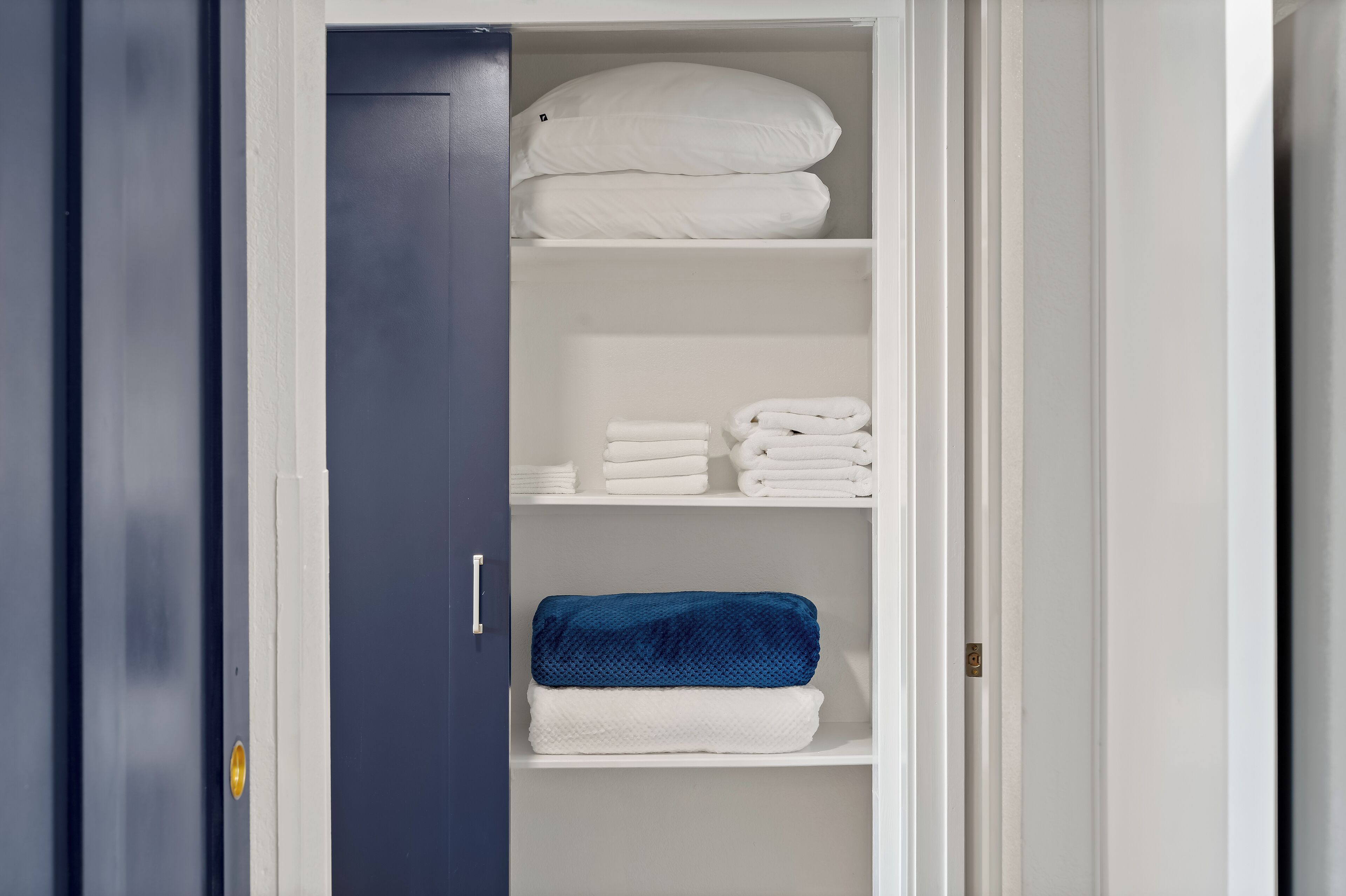 Un placard avec plusieurs étagères, dont certaines contiennent des serviettes pliées et une couverture bleue.