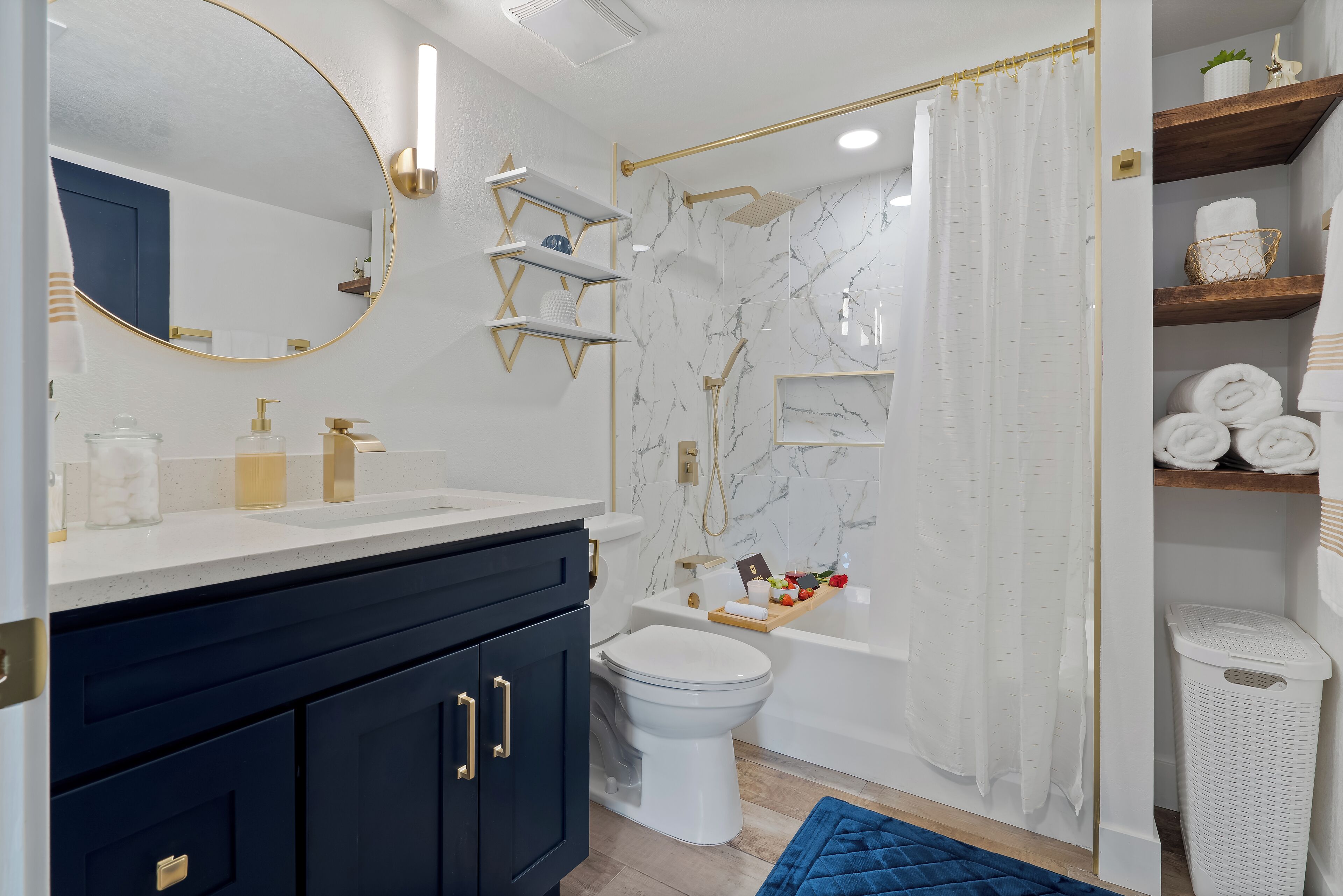 Ein modernes Badezimmer mit einer weißen Marmordusche, einer weißen Toilette und einem dunkelblauen Waschtisch mit goldfarbenen Griffen.