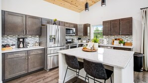 A modern kitchen with dark cabinets, stainless steel appliances, and a central island with two bar stools. - Mountain & Pond Views, Hot Tub, Stargazing, Kid + Dog Friendly, Loft+3BR (Florissant)