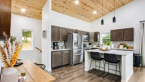 A modern kitchen with wooden ceiling, stainless steel appliances, and a central island with bar stools. - Mountain & Pond Views, Hot Tub, Stargazing, Kid + Dog Friendly, Loft+3BR (Florissant)