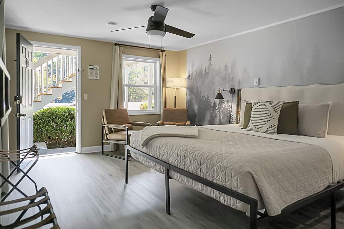 Ein Schlafzimmer mit einem Bett, zwei Stühlen, einem Deckenventilator, einem Fenster und einer Tür zu einer Treppe.
