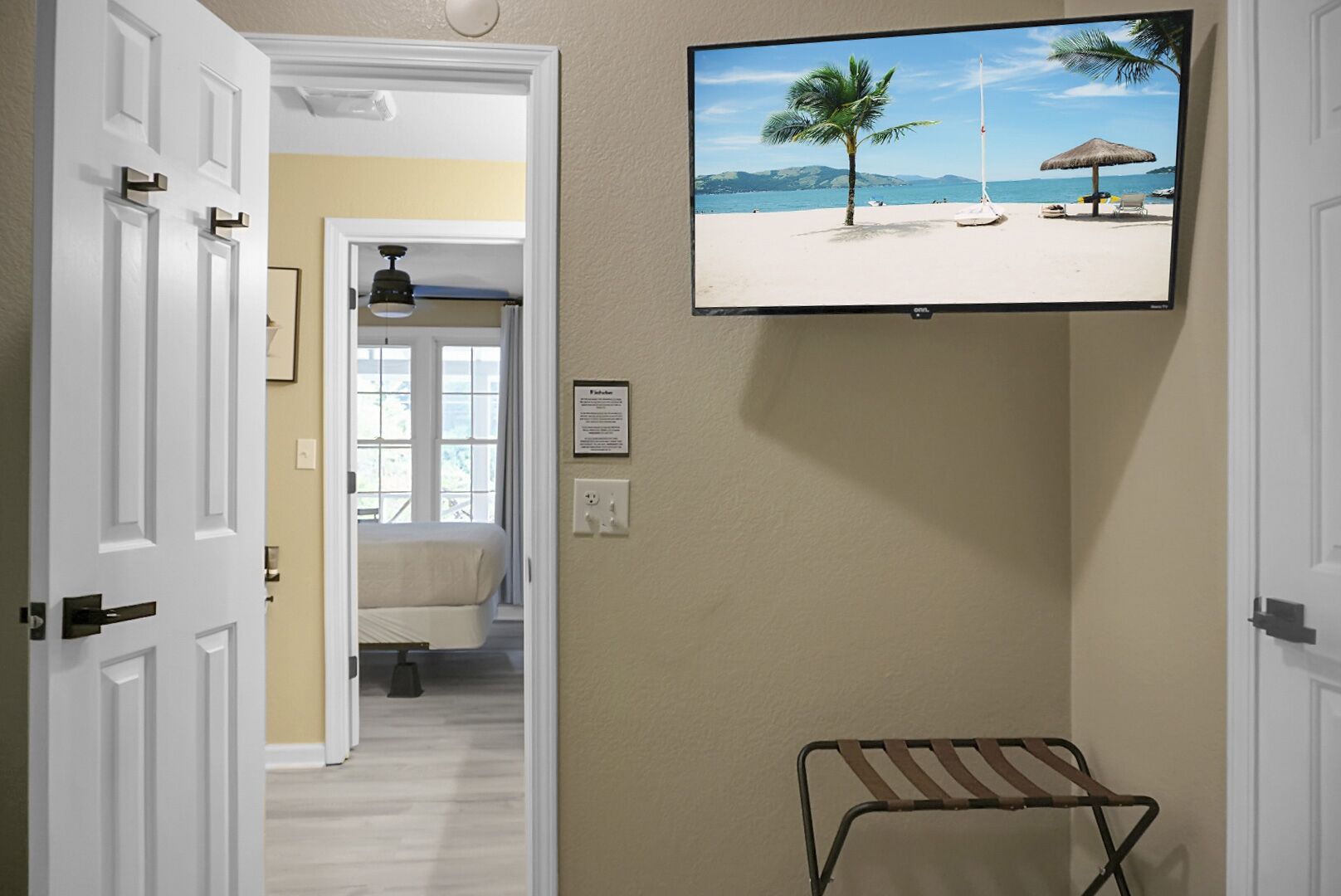 Een hotelkamer met een televisie waarop een strand te zien is, een bed, een stoel en een klein tafeltje.