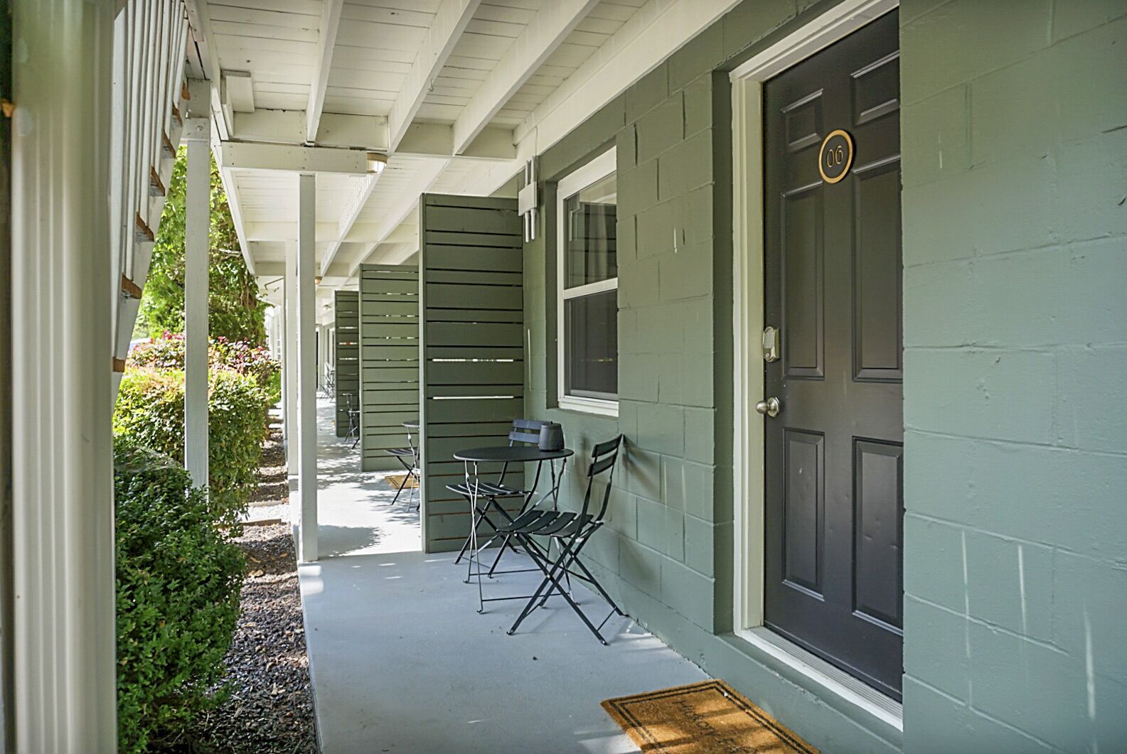 A covered porch with a table and chairs, a door with a number, and a window.