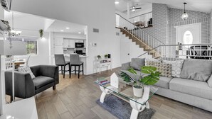Ein modernes Wohnzimmer mit Glastisch, grauem Sofa und einer Treppe, die zu einem Erker führt.