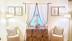 A room with two wicker chairs, a wooden cabinet, and a window with curtains. - Walking distance to Betsie River & 10 minutes to Lake Michigan & Crystal Mnt! (Benzonia)