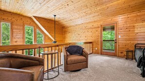 A cozy cabin interior with a wooden ceiling, a balcony with a railing, a sofa, a chair with a blanket, and a small table. - Mountain Vacation Time! 2 miles to GSMNP@ Line Springs~Hot Tub~Games~2 Decks (Sevierville)