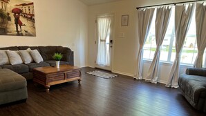 A living room with a dark wood floor, a brown leather sofa, a wooden coffee table with a plant, and a painting on the wall.