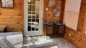 A wooden interior with a glass door, a small console table with decorative items, and a window with blinds.