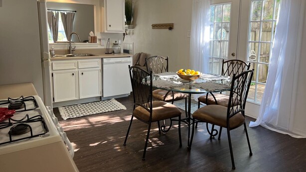 A compact kitchen with white cabinetry, a gas stove, and a dining area with a glass table and four chairs.