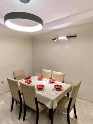 A dining area with a round table set for six, six chairs, and a modern pendant light fixture above. - Charming 3-Bed Apartment in 7th circle Amman (Amman)