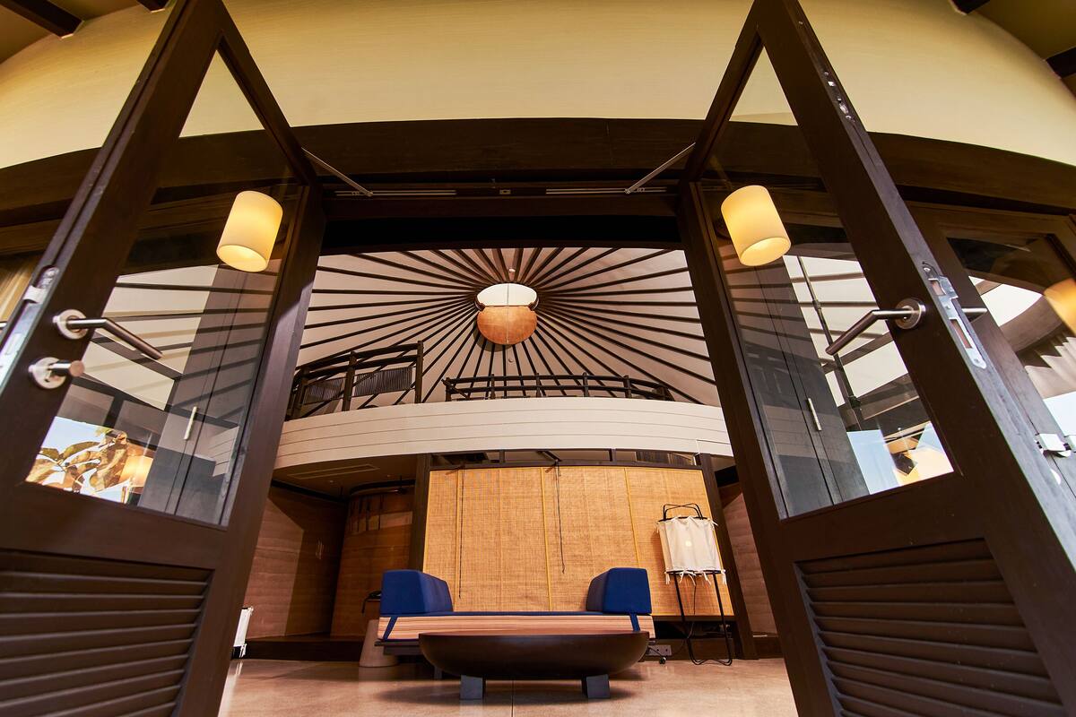 A modern interior with a central seating area, a unique ceiling design, and a large window.