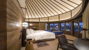 Una habitación de hotel moderna con techo curvo, una cama grande, un escritorio y vistas al exterior.