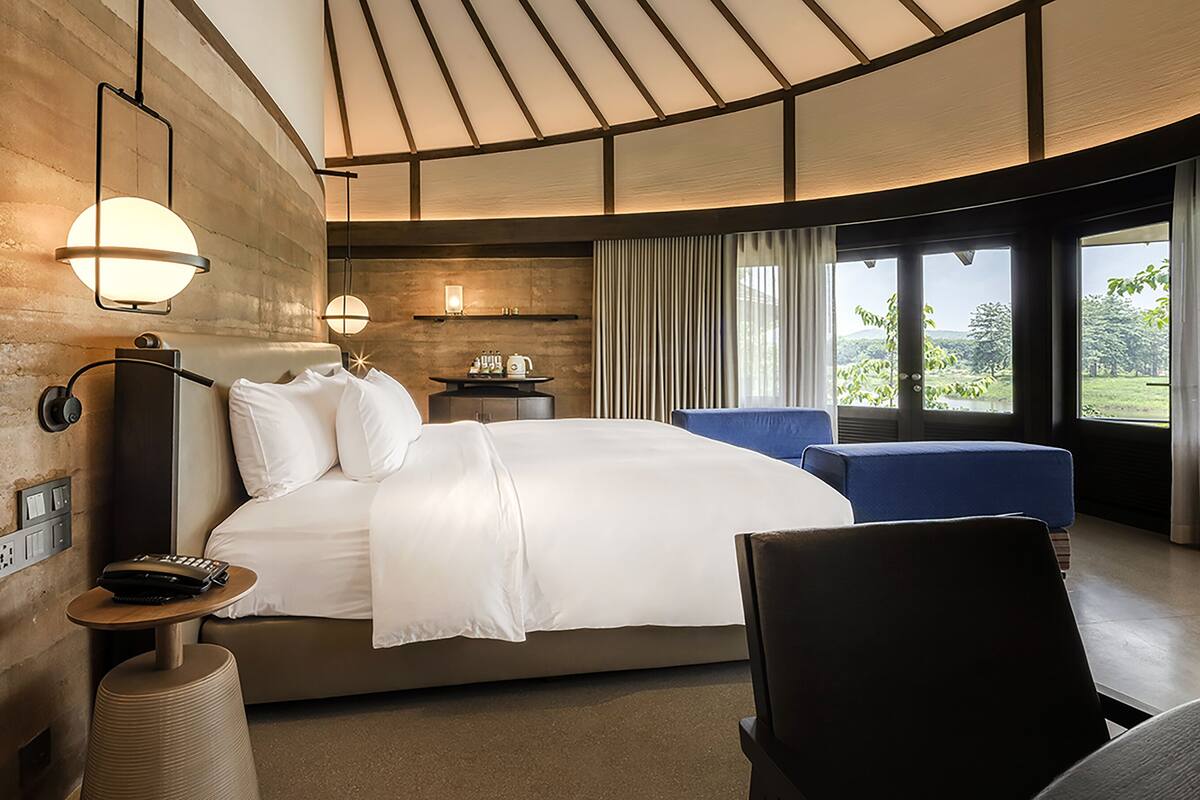 A modern hotel room with a large bed, a desk, a chair, and a view of the outdoors.