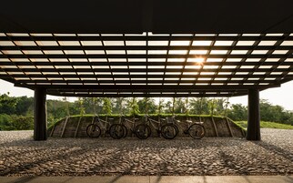 Un área de estacionamiento para bicicletas cubierta, con suelo de grava y una pérgola de madera.