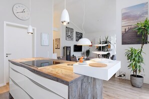 A modern kitchen with a wooden countertop, white cabinetry, pendant lighting, and a large potted plant.