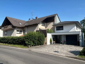 Uma casa de dois andares com garagem, telhado inclinado e um jardim bem cuidado.