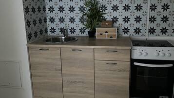 Een koelkast, een oven, een kookplaat, kookgerei, borden en bestek