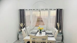 A dining area with a table set for four, surrounded by white chairs, with a view of a building through sheer curtains. - mounting view and popular for hiking area (Desert Hot Springs)