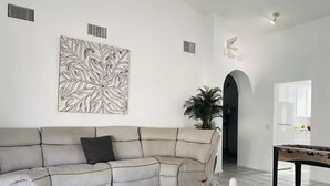 A modern living room with a beige sectional sofa, a glass coffee table with decorative items, a foosball table, and a large abstract wall art piece. - mounting view and popular for hiking area (Desert Hot Springs)