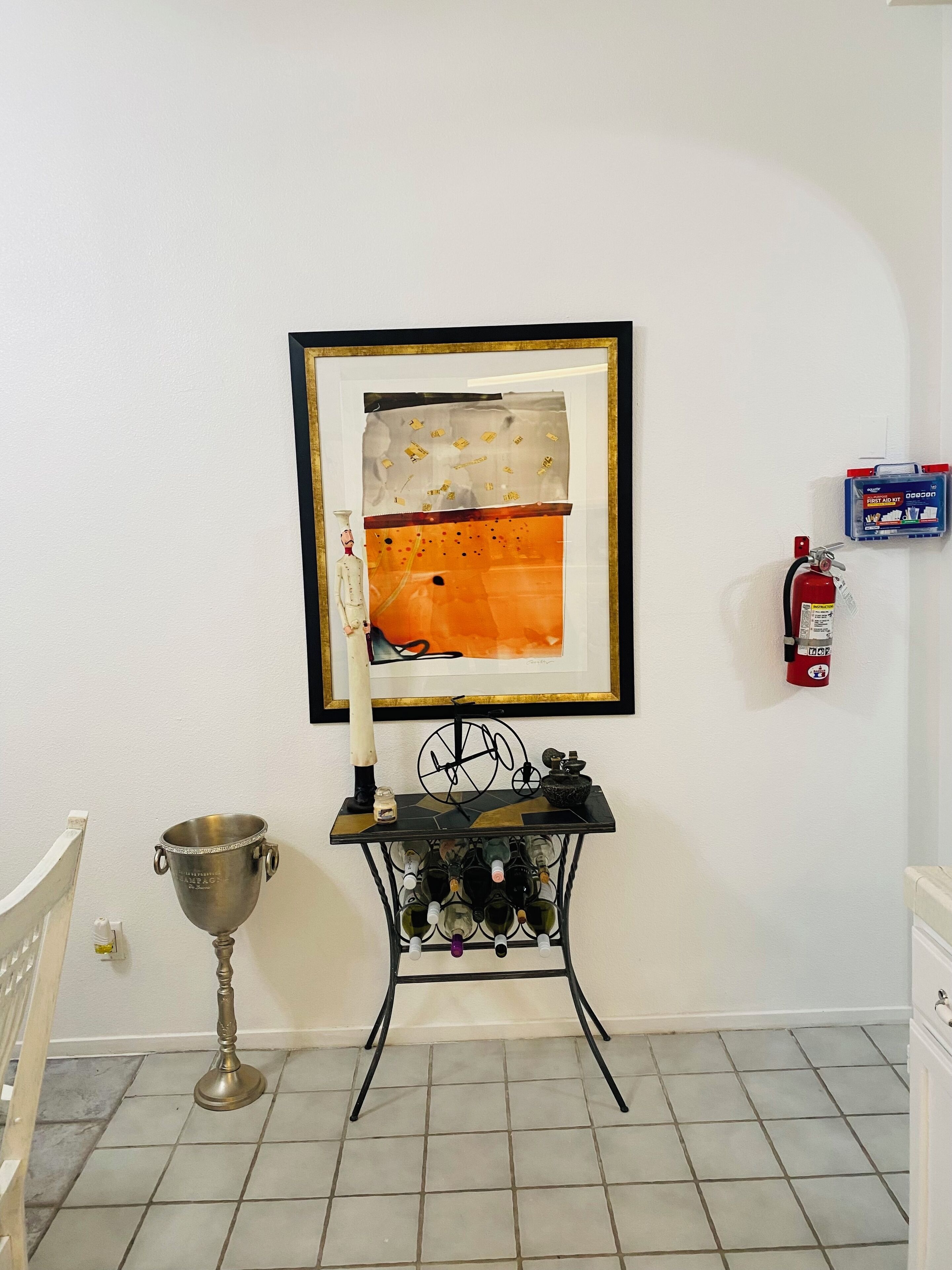 A room with a framed abstract painting, a wine rack, a metal trophy, and a fire extinguisher on the wall.