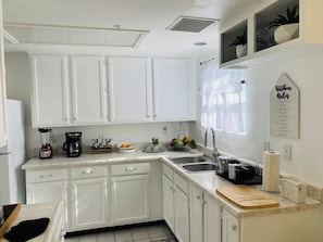 A kitchen with white cabinets, a coffee maker, a sink, and a wall-mounted sign.