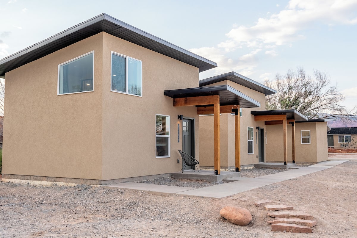 A modern two-story house with a beige exterior, large windows, and a covered patio area.