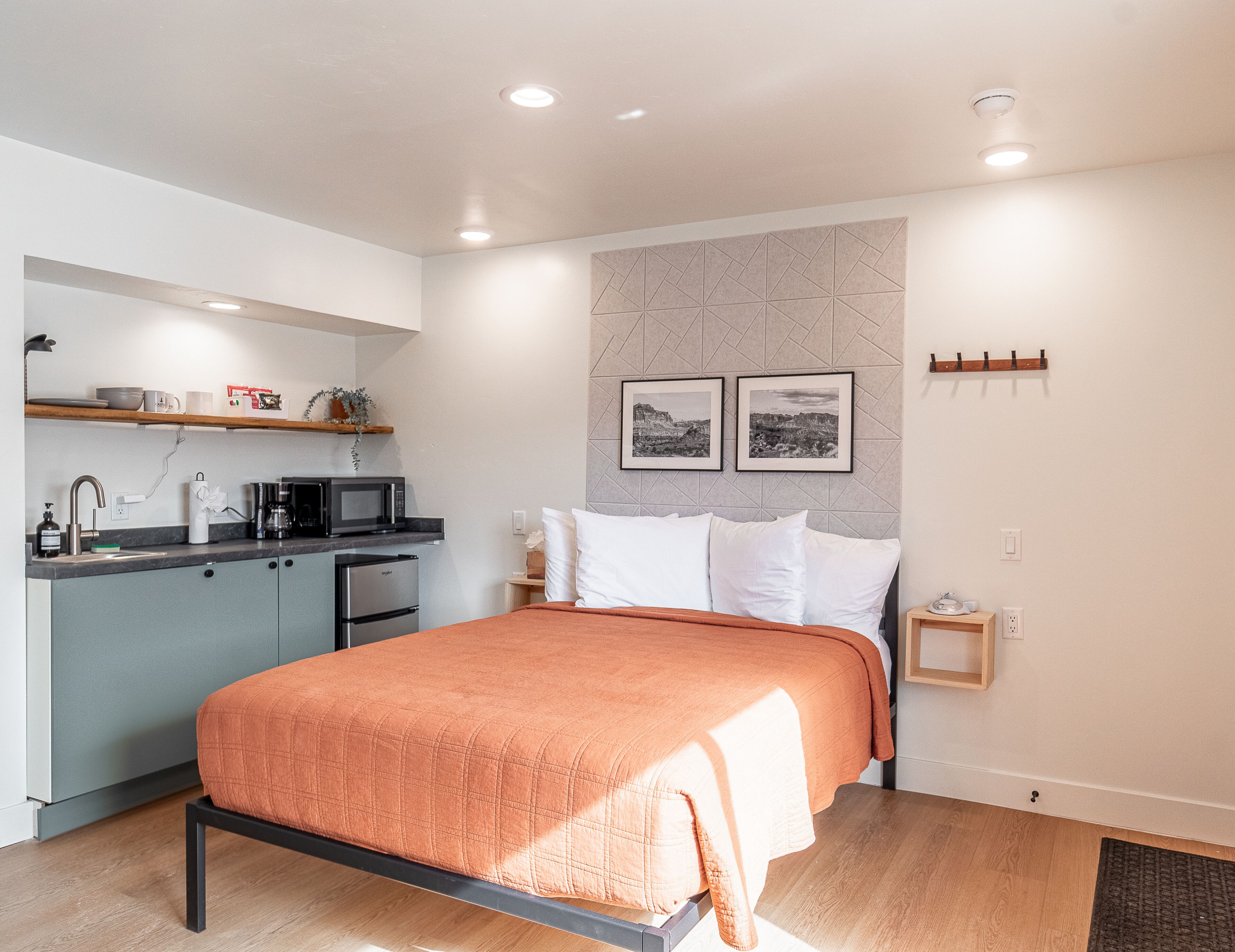 Une chambre moderne avec un lit, une petite kitchenette et une étagère fixée au mur.