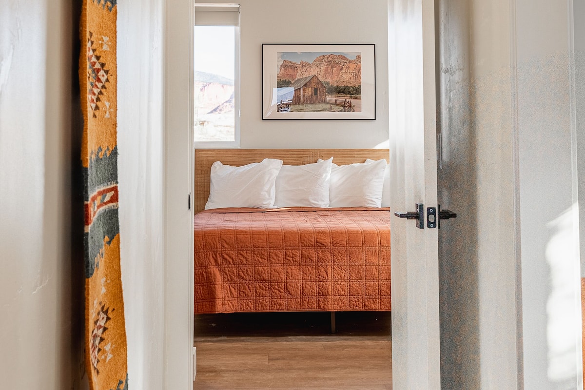 A bedroom with a bed, a window, and a painting on the wall.