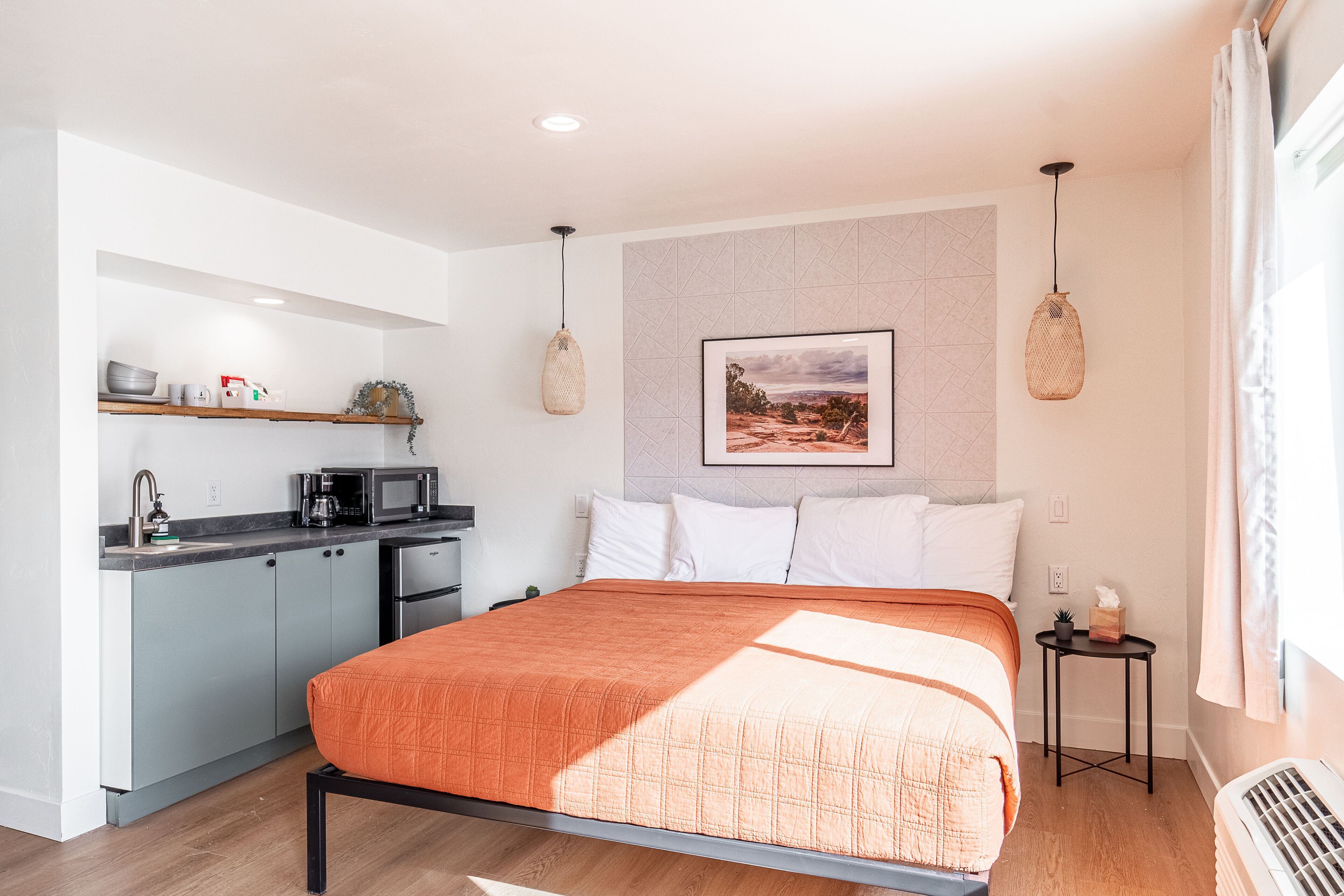 A modern bedroom with a large bed, a kitchenette, and a bathroom.