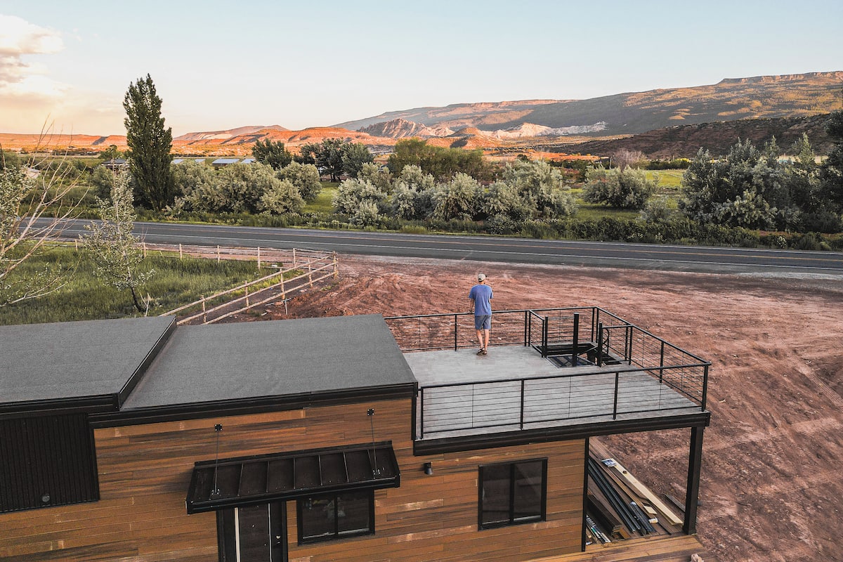 A modern building with a flat roof, a balcony, and a view of a road and hills in the distance.