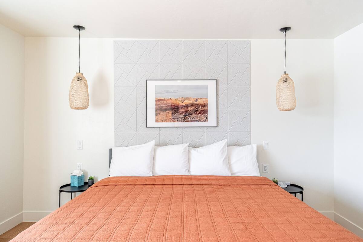 A bedroom with a bed, a framed picture on the wall, and two hanging light fixtures.