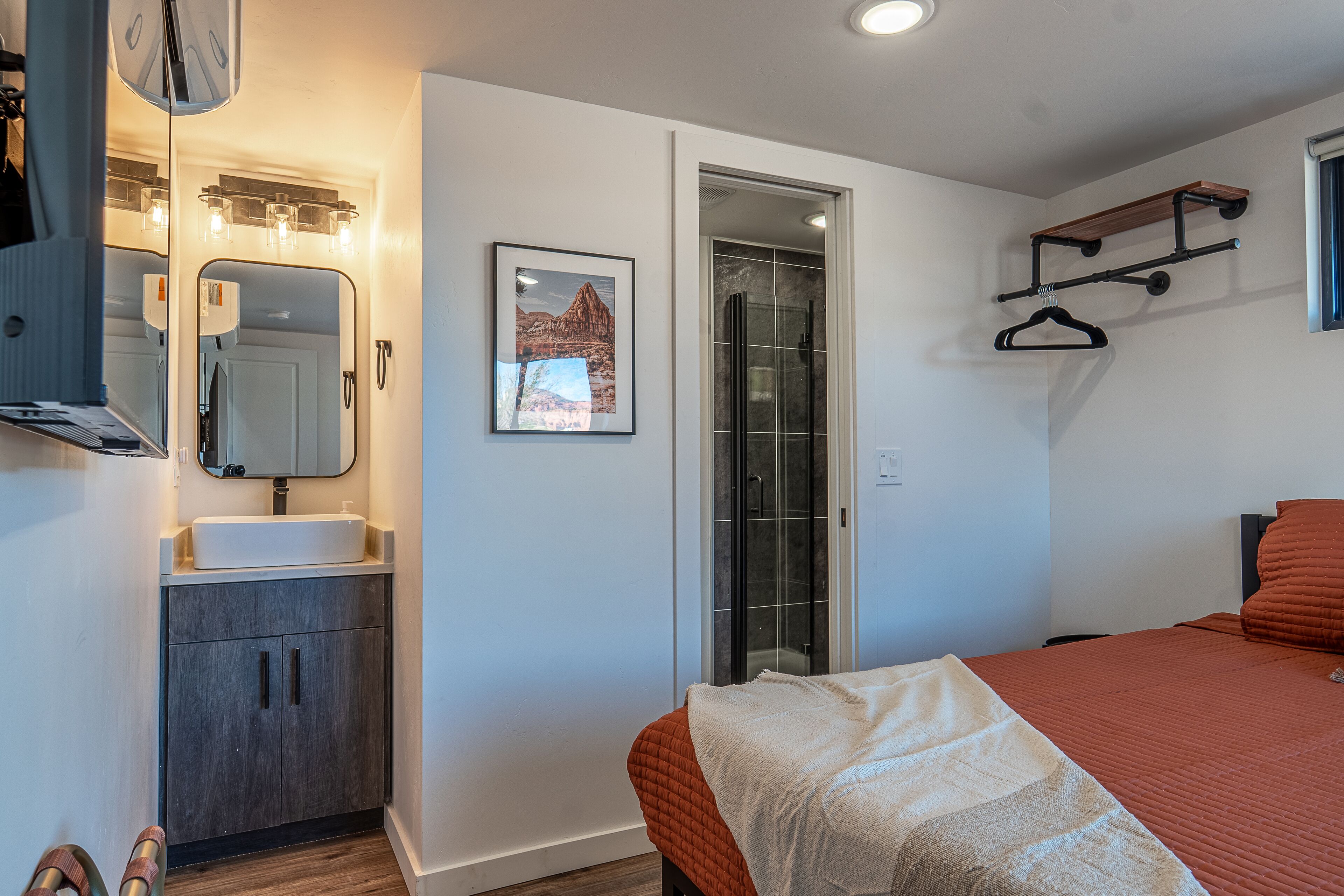 A bedroom with a bed, a bathroom with a mirror, a sink, and a shower.
