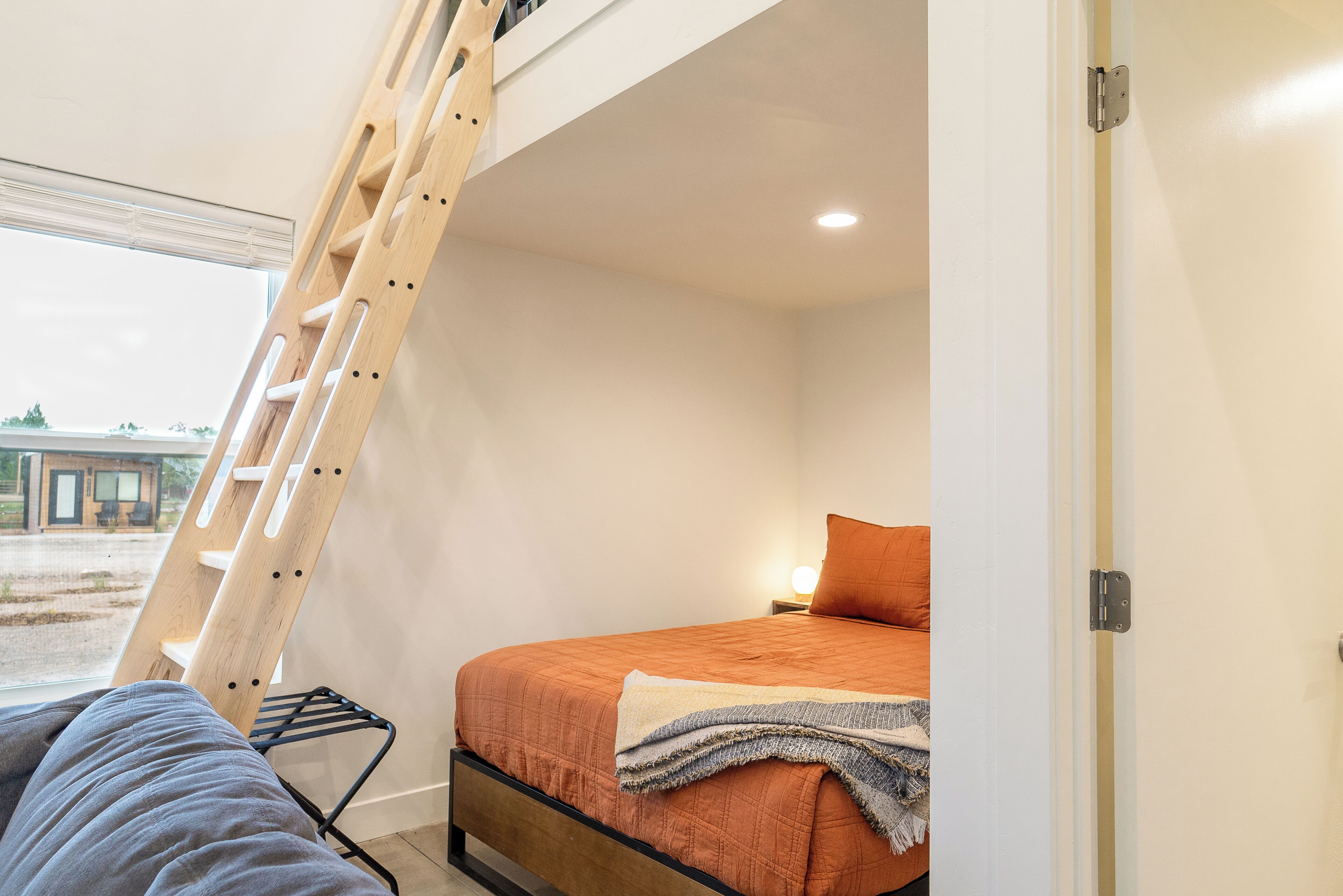 A bedroom with a bed, a ladder, and a window.