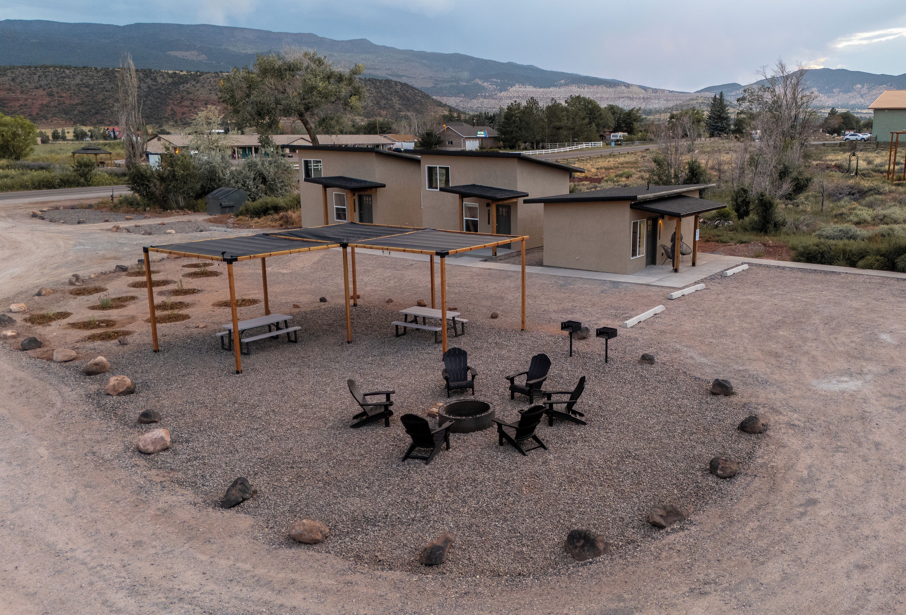 A campground with a covered seating area, fire pit, and outdoor chairs.