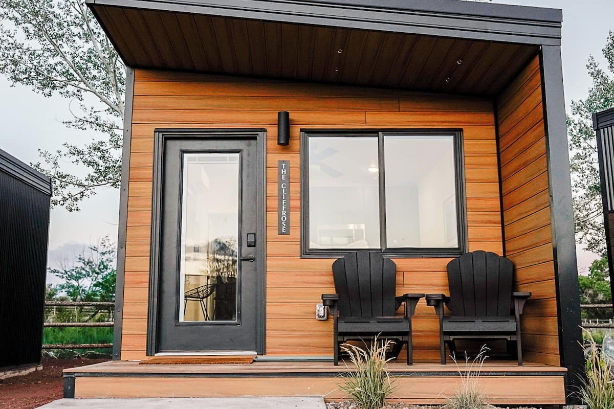 A modern building with a wooden facade, a black door, and two black Adirondack chairs on the porch.