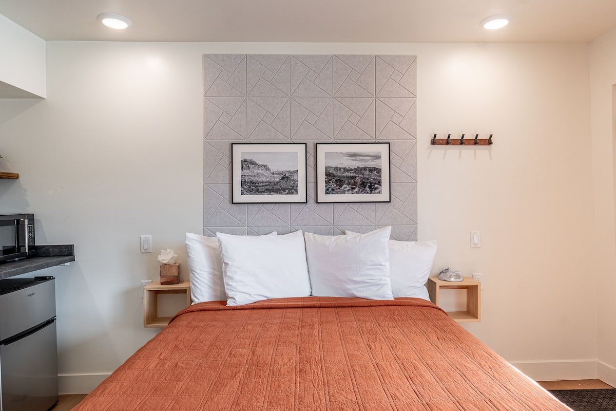 A neatly arranged hotel room with a bed, two bedside tables, a microwave, and a small refrigerator.