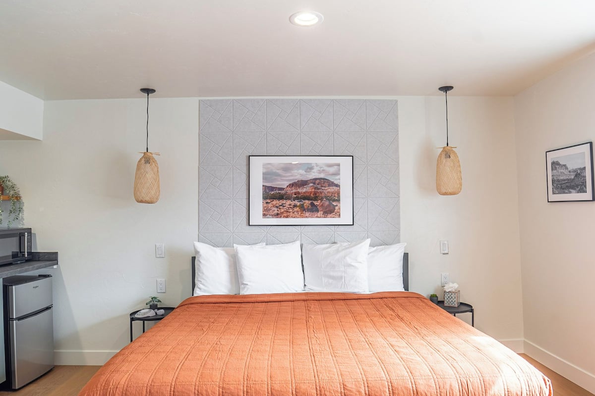 A hotel room with a bed, a small kitchenette, and a framed picture on the wall.