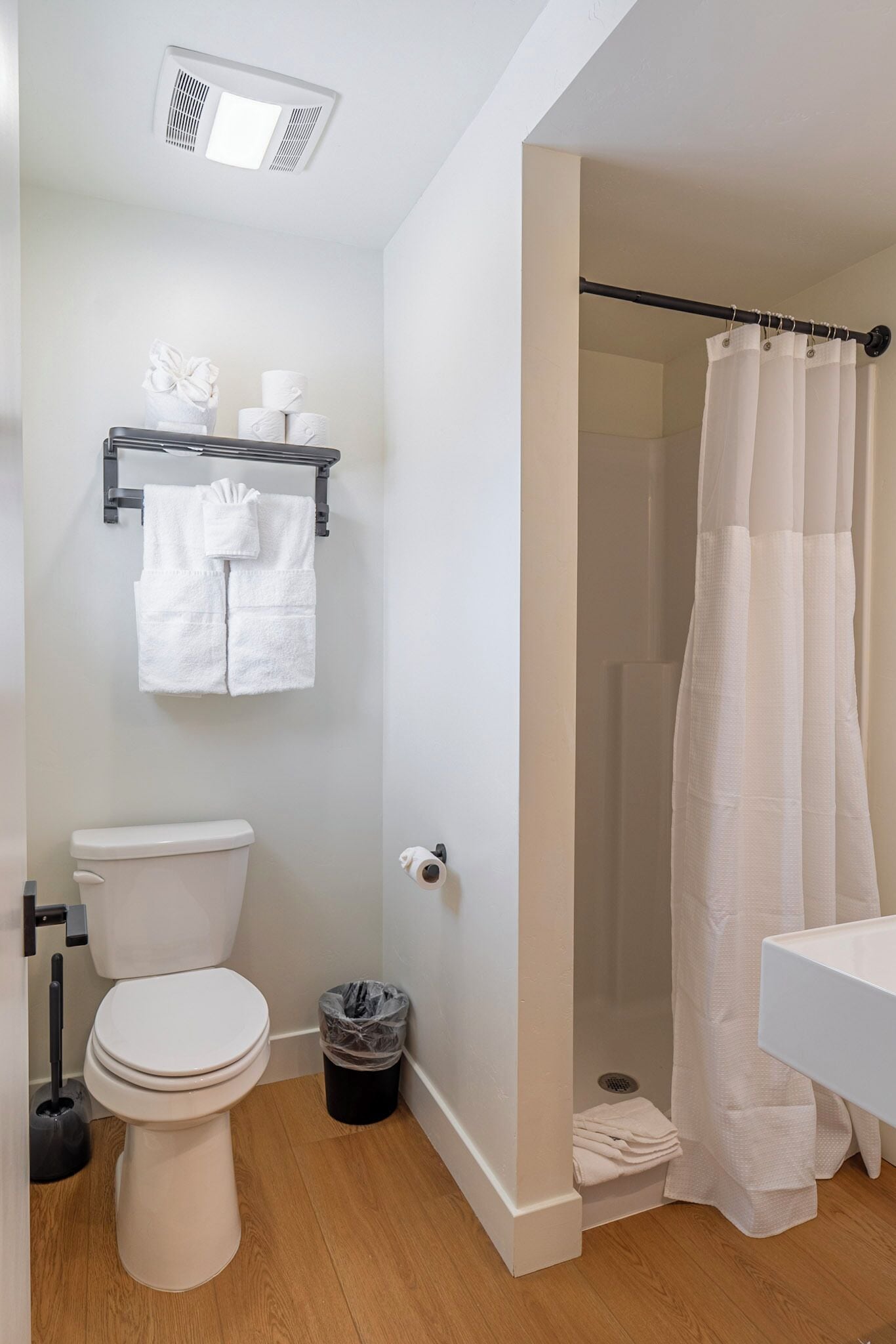 A bathroom with a toilet, a shower curtain, a sink, and a trash bin.