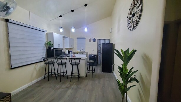 Una cocina compacta con una isla central, taburetes de bar, un refrigerador y un reloj en la pared.