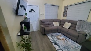 Una sala de estar con un sofá modular, una mesa de centro, una planta en maceta y una puerta con ventanal.